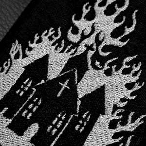 Può includere: Toppa ricamata nera con un design gotico. Raffigura un edificio in fiamme con una croce in cima, circondato da fiamme. Il ricamo bianco risalta sullo sfondo nero, creando un'immagine dettagliata. Ideale per giacche, borse o altri articoli in tessuto.
