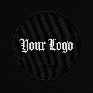 Może przedstawiać: Czarna, okrągła naszywka z wyhaftowanym napisem "Your Logo" w białej, gotyckiej czcionce. Naszywka ma czarną obwódkę i jest umieszczona na czarnym tle.