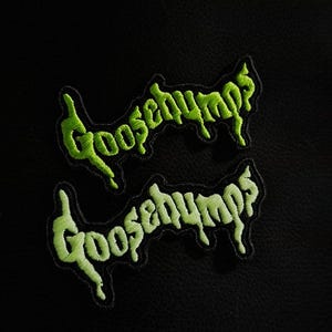 Może przedstawiać: Dwie zielone, haftowane naszywki z napisem "Goosebumps". Napis jest w stylizowanej czcionce. Naszywki są na czarnym tle. Wymiary: 5 cm wysokości i 9,5 cm szerokości.