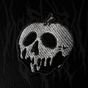 Peut inclure: Écusson brodé noir et blanc représentant un crâne dans une pomme. Le crâne est noir, contrastant avec le blanc de la pomme. Le fond est une surface noire texturée.