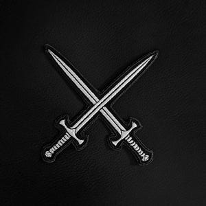 Pode incluir: Patch bordado preto com duas espadas brancas cruzadas. As espadas têm cabos e lâminas detalhadas, sobre um fundo preto texturizado. Ideal para adicionar a roupas ou acessórios.