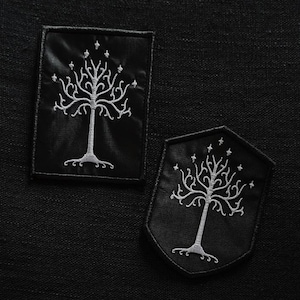 Peut inclure: Deux écussons noirs brodés avec un motif d'arbre blanc. L'un est rectangulaire, l'autre en forme de bouclier. L'arbre a une couronne et des racines détaillées. Fond sombre et texturé.