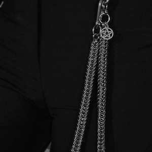 May include: Silver-toned chain wallet accessory with a carabiner clip and a pentagram charm. The chain is made of small, interlocking metal rings. The accessory is designed to attach to a belt loop or other clothing item.