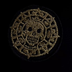 Può includere: Toppa circolare con un teschio dorato, circondato da un intricato motivo dorato, su sfondo nero. Il teschio presenta dettagli. Adatto per abbigliamento o accessori.