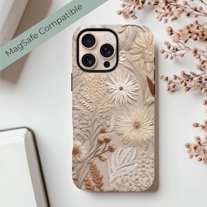 May include: A beige phone case with a floral design. The case features a raised, textured pattern of flowers, leaves, and stems in varying shades of beige and brown. The words "MagSafe Compatible" are printed on the case.