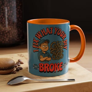 Puede incluir: Taza de cerámica turquesa con interior y asa naranja. La taza presenta el texto "I FIX WHAT YOUR DIY BROKE" con una ilustración de un reparador. Una cuchara y un macaron están en primer plano.