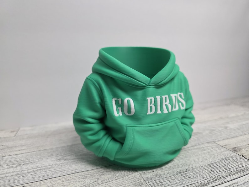 May include: A green hoodie with the words "GO BIRDS" in white block letters across the chest. The hoodie has a front pocket and a hood. The garment is made of a soft material.