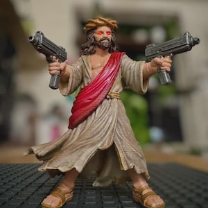 May include: A painted figurine of a bearded figure wearing a crown of thorns and a tan robe with a red sash. The figure has glowing red eyes and is holding a dark gray handgun in each hand. The figure wears brown sandals on their feet.