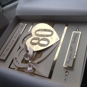 May include: A white card with gold accents and a gold glitter heart with the number 80 inside. The card says "To my Lovely Husband Phil" and "On your 80th Birthday".