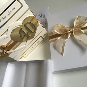 May include: A white card with gold accents and a gold heart with the number 40 on it. The card says "To a special Son Graeme" and "On your 40th Birthday". The card is in a white box with a gold ribbon.