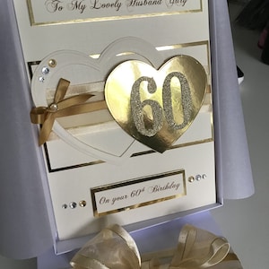 May include: A white card with gold accents and a gold heart with the number 60 in it. The card says "To My Lovely Husband Gary" and "On your 60th Birthday".