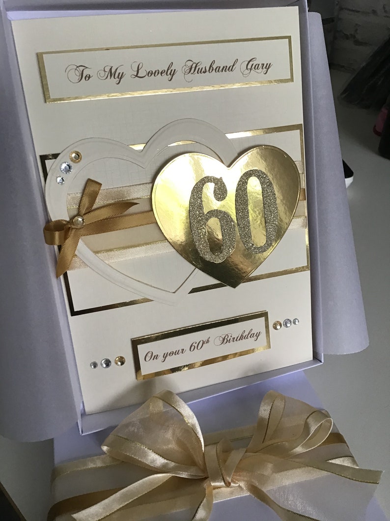 May include: A white card with gold accents and a gold heart with the number 60 in it. The card says "To My Lovely Husband Gary" and "On your 60th Birthday".