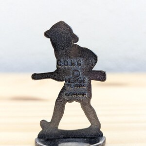 May include: A dark metal figurine of a person walking, with a hat and a stick. The figurine is on a round base. The text "CONG 1", "HERGE TL1984 CORNER" is visible on the figurine.