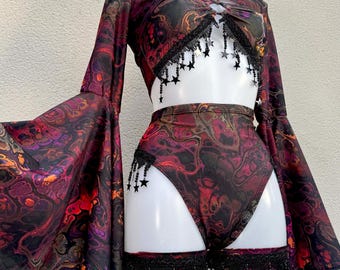 May include: A two-piece outfit featuring a long-sleeved crop top with flared sleeves and high-waisted bottoms, both in a dark marbled print of black, red, and orange. The set is accented with black fringe trim and dangling black star charms.