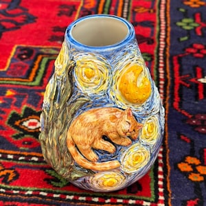 May include: A ceramic vase with a design inspired by Van Gogh's "Starry Night." The vase features a sleeping ginger cat, yellow stars, and a crescent moon. The background is a swirling blue and yellow pattern.