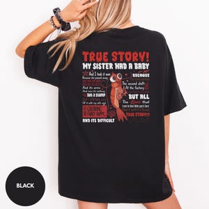 May include: A black t-shirt featuring a graphic on the back with red and white text that reads TRUE STORY! MY SISTER HAD A BABY and a narrative about a shrimp. The design includes a cartoon shrimp illustration, coral accents, and wavy lines.