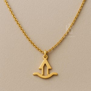Op de afbeelding: Een goudkleurige ketting met een hanger met een gestileerde pijl en een gebogen basis. De hanger hangt aan een fijne ketting. De sieraden zijn geplaatst tegen een neutrale achtergrond.