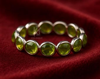 Könnte beinhalten: Ein silberner Ring mit oval geschliffenen, hellgrünen Edelsteinen, die in einem durchgehenden Band angeordnet sind. Der Ring wird auf rotem Samt präsentiert. Der Text "KING JEWELRY" ist sichtbar.
