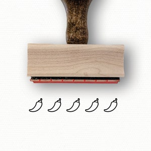 May include: A wooden rubber stamp with a brown handle and a red ink pad. The stamp features a design of five chili peppers.
