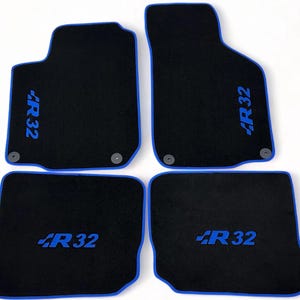 May include: Set of four black car floor mats with blue trim. Each mat features the text "R32" in blue. The mats are designed to fit the front and rear footwells of a vehicle.