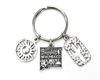 May include: Silver keyring with three charms: a sun, a state of New Mexico outline with the cities Santa Fe, Albuquerque, and Carlsbad, and a cactus.