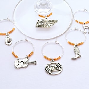 Puede incluir: Conjunto de seis charms para copas de vino en plata con cuentas naranjas. Los charms representan una guitarra, una bota, una nota musical, un sombrero de vaquero y el estado de Tennessee.