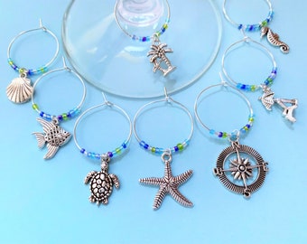 May include: Set of six silver-tone glass charms with blue and green beads. The charms include a seashell, a fish, a turtle, a starfish, a compass, and a palm tree.