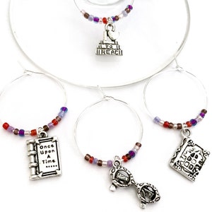 May include: Set of four silver wine glass charms with colorful beads. Each charm features a different fairytale theme: a book with the text "Once Upon A Time...", a castle, a glass slipper, and a heart with the text "To Reach".
