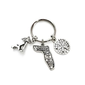 May include: Silver keychain featuring a Florida state outline charm with the text "Tallahassee Florida" and city names, a seashell charm, and a miniature beach umbrella charm.