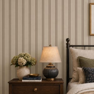 Può includere: Un comodino in legno scuro con tre cassetti e pomelli in ottone, sormontato da un vaso beige testurizzato con ortensie verdi, una piccola ciotola dorata, due libri intitolati The Kinfolk Home e This is Home e una lampada con base a coste.