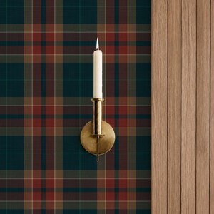 May include: A brass wall sconce holding a single white taper candle, mounted against a dark green, red, and tan plaid wallpaper pattern. The sconce features a circular backplate and a cylindrical candle holder, positioned beside vertical wood paneling.