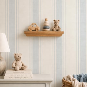 Op de afbeelding: Een houten zwevende plank met een houten speelgoedauto, een stapelringspeeltje en een kleine teddybeer. Daaronder staat een lichtgrijze ladekast met een lamp, een teddybeer en drie boeken getiteld Goodnight Moon, Guess How Much I Love You en The Wonderful Things You Will Be.