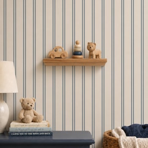 Op de afbeelding: Een muur met beige en blauw verticaal gestreept behang, een houten plank met een houten auto, een stapelspeeltje en een leeuwenfiguur. Daaronder staat een donkerblauwe ladekast met een teddybeer en boeken Guess How Much I Love You.