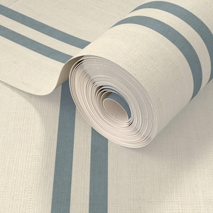 Op de afbeelding: Een rol gebroken wit textiel met een geweven structuur en twee parallelle leiblauwe strepen die verticaal over de lengte van het materiaal lopen. De stof is gedeeltelijk uitgerold en toont het consistente patroon en de strakke rol.