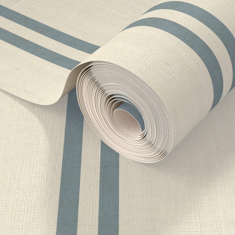 Op de afbeelding: Een rol gebroken wit textiel met een geweven structuur en twee parallelle leiblauwe strepen die verticaal over de lengte van het materiaal lopen. De stof is gedeeltelijk uitgerold en toont het consistente patroon en de strakke rol.