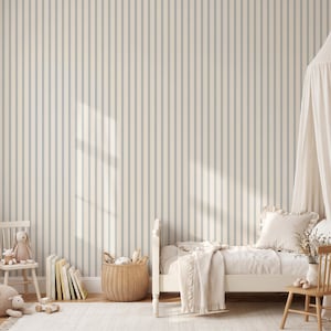 Op de afbeelding: Behang met een herhalend patroon van dunne, verticale blauwe strepen op een cr&egrave;mekleurige achtergrond. Het ontwerp bedekt een muur achter een bed met wit beddengoed, een rieten mand, een houten stoel en een verzameling boeken.