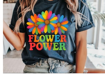 May include: A navy blue t-shirt featuring three colorful flower graphics with rainbow petals and brown centers. The text "FLOWER POWER" is printed in vibrant rainbow colors below the flowers. The shirt is a casual style.