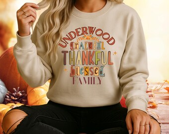 Könnte beinhalten: Beigefarbenes Sweatshirt mit dem Text "UNDERWOOD grateful THANKFUL blessed FAMILY" in bunten, herbstlichen Buchstaben. Das Sweatshirt hat eine neutrale Farbe, passend für den Herbst. Das Design enthält orange, braune und grüne Akzente, die Dankbarkeit und Familie vermitteln.