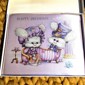 Könnte beinhalten: Eine Grußkarte in einer weißen Box mit dem Text "HAPPY BIRTHDAY TO MY WIFE". Die Karte zeigt eine Illustration von zwei anthropomorphen Kaninchen in einer Badewanne, mit lila und lavendelfarbenen Tönen.