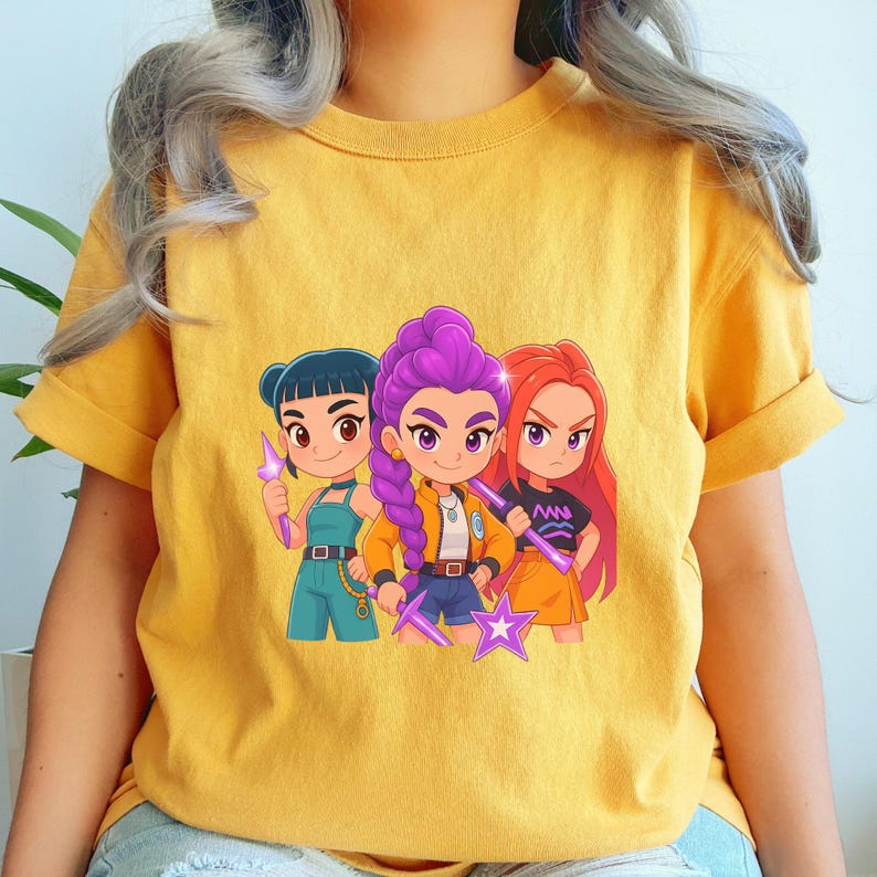 May include: Yellow t-shirt featuring a cartoon illustration of three girls with different hair colors and outfits. The girls are holding tools and a star. The illustration is in a cartoon style.