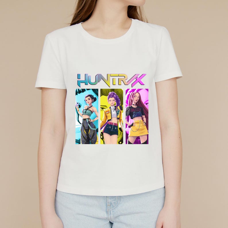 May include: White t-shirt featuring a colorful graphic of three stylized female figures with the word "HUNTR/X" above them. The graphic has a vibrant, digital art style with a gradient color scheme.