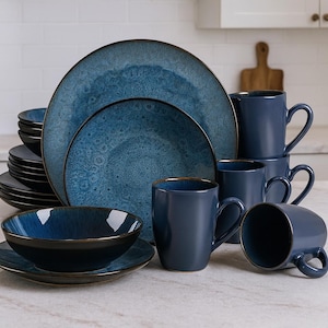 May include: A set of blue ceramic tableware, including plates, bowls, and mugs. The plates and bowls feature a textured, speckled pattern. The mugs are stacked and arranged with the plates, creating a coordinated kitchenware set.