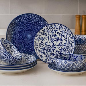May include: A set of blue and white ceramic dinnerware, including plates and bowls. The plates display detailed patterns, with some featuring a geometric design and others a floral motif. The bowls are stacked, and the set is arranged on a white surface.