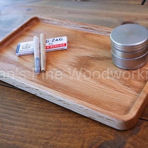 May include: A wooden rolling tray with a curved edge, holding two pre-rolled cigarettes, a pack of G-ZAG 1 1/4 rolling papers, and a silver metal grinder. The tray is made of light brown wood.