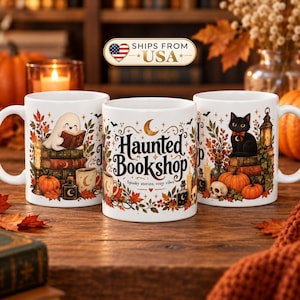 May include: Three white ceramic mugs featuring colorful autumn-themed illustrations. The center mug displays the text "Haunted Bookshop" and "Spooky stories, cozy vibes" surrounded by pumpkins, leaves, a ghost, a black cat, and books.