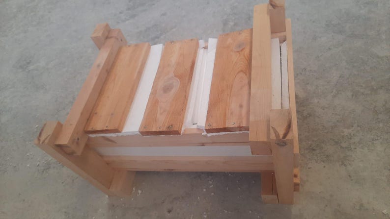 Puede incluir: Un peque&ntilde;o banco de madera sin terminar con un marco rectangular y un asiento de listones. El banco est&aacute; construido con madera de color claro y presenta un dise&ntilde;o simple y r&uacute;stico. El asiento est&aacute; hecho de tablones de madera con espacios blancos.