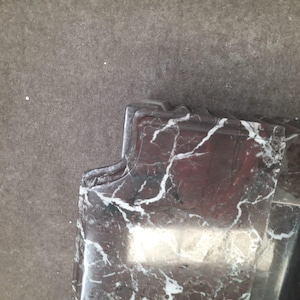 May include: Close-up of a section of a marble object with a dark red base color and white veining. The object has a decorative, curved edge. The background is a solid, neutral gray color.