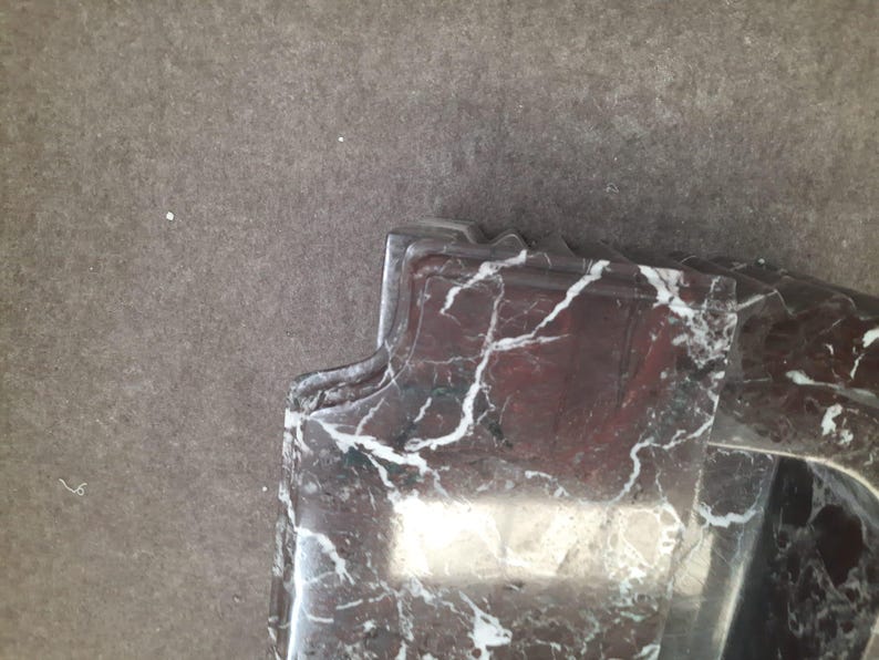 May include: Close-up of a section of a marble object with a dark red base color and white veining. The object has a decorative, curved edge. The background is a solid, neutral gray color.