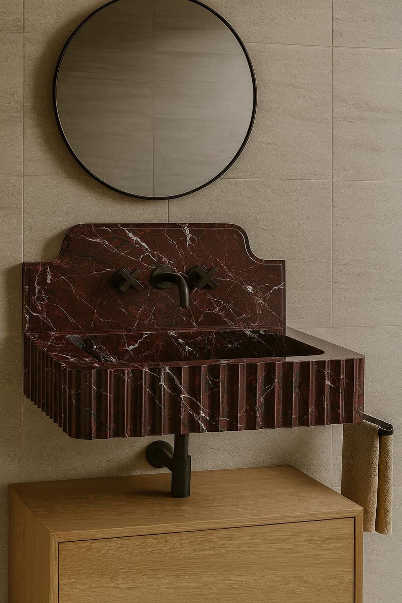May include: A wall-mounted bathroom sink with a deep red marble finish and white veining. The sink has a fluted front and black fixtures, including a faucet and cross-shaped handles. A round black mirror hangs above.
