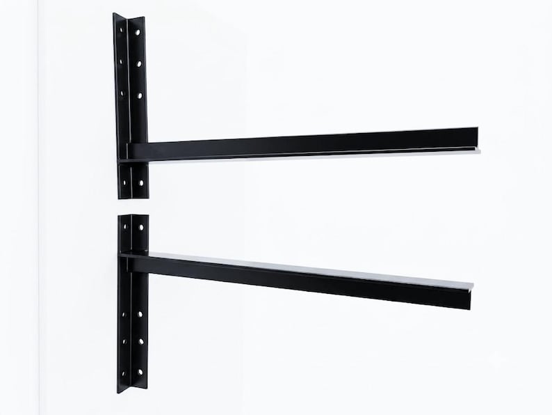 Puede incluir: Dos soportes de estante de metal negro en forma de L, con una placa de montaje vertical con cuatro orificios circulares preperforados y un brazo de soporte horizontal. Los soportes tienen un acabado mate liso y un dise&ntilde;o estructural r&iacute;gido.